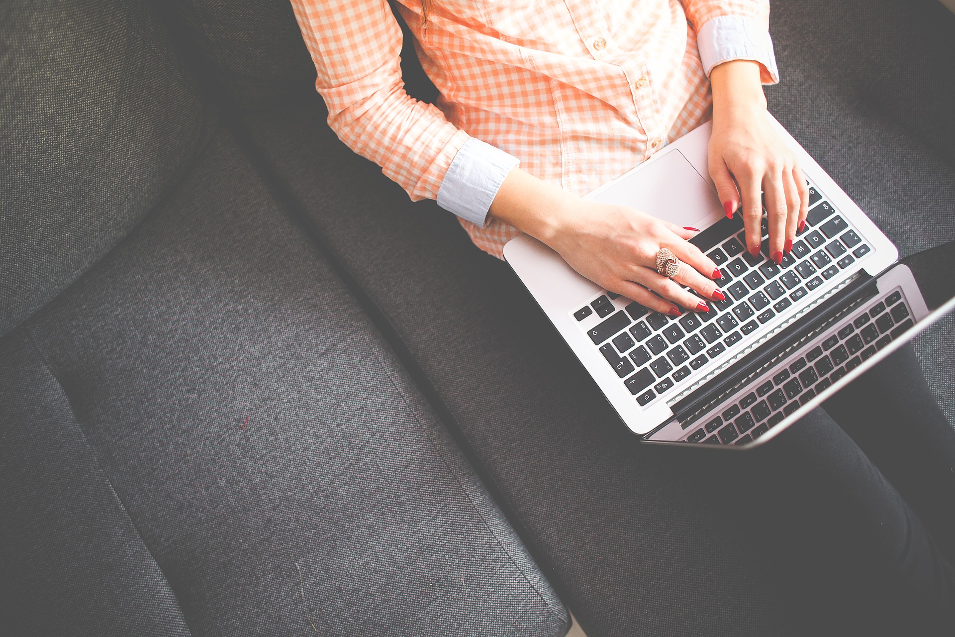 Person sitzt auf einem Sofa mit dem aufgeklappten Laptop auf den Beinen
