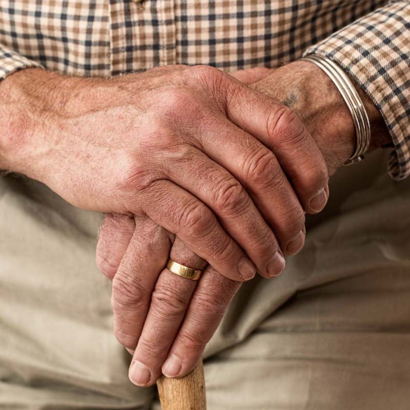Die Hände eines älteren Menschen stützen sich gefaltet auf einen Stock.